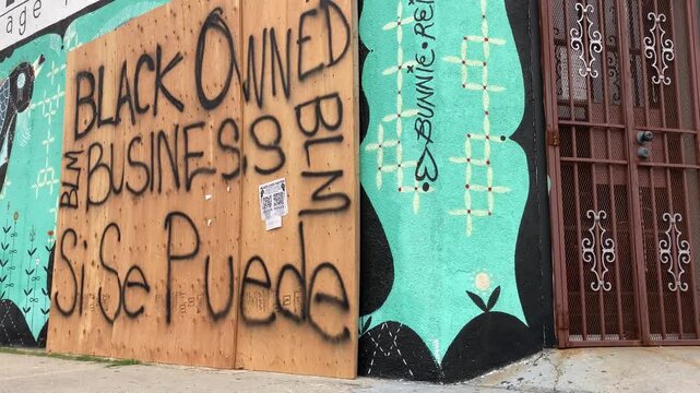 Boarded up storefront with graffiti murals in urban environment.