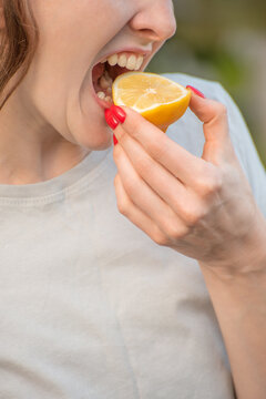 Woman opening her mouth wide, bringing a fresh, half cut lemon to her lips, and reacting to the intense, tart flavor of the citrus fruit with an expressive face