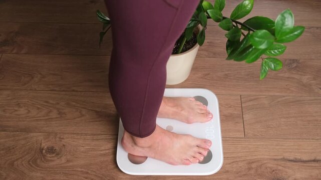 Woman stepping onto digital bathroom scale at home. Barefoot legs measuring body weight. Weight loss control, diet and healthy lifestyle fitness monitoring concept