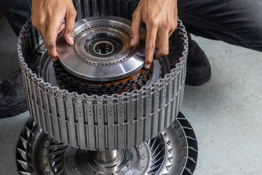 Mechanic assembling automatic transmission clutch pack plates and torque converter drum components manually.