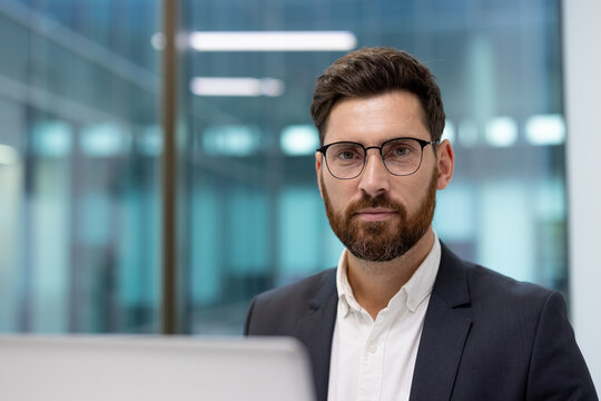 Close-up portrait of a young businessman in glasses and a suit in the office, looking at the camera