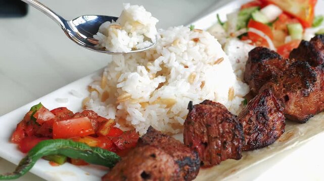 Serving rice with a spoon on a plate full of delicious grilled meat and salad