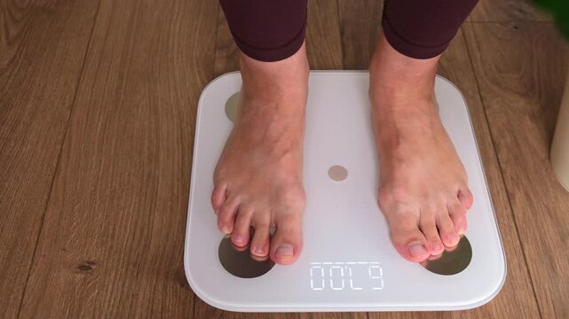 Close-up of woman feet standing on digital smart bathroom scale measuring body weight. Weight loss control and diet concept. Healthy lifestyle and fitness tracking at home