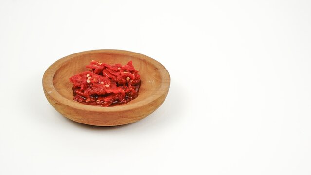 Freshly ground Indonesian red chili paste served in a small traditional wooden bowl, isolated on a white background.