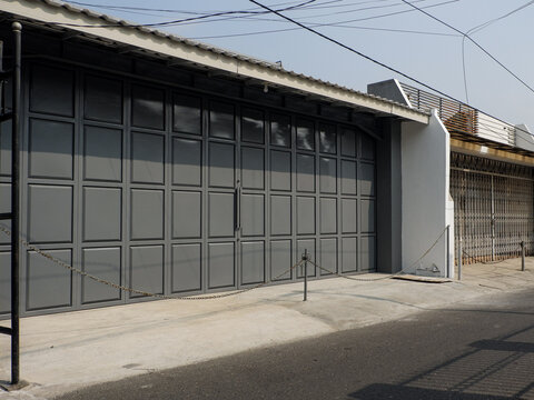 Modern grey folding steel gate featuring square panel design on a house garage frontage under bright sunlight.