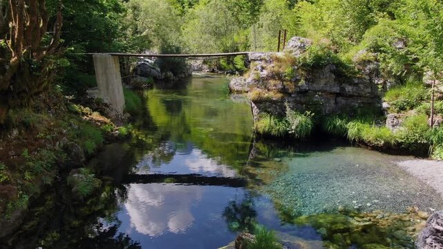 The Stunning River Path to Albania's Blue Eye: Stunning natural landscape showing a clear turquoise river flowing under a small wooden bridge in a lush green forest on a sunny day