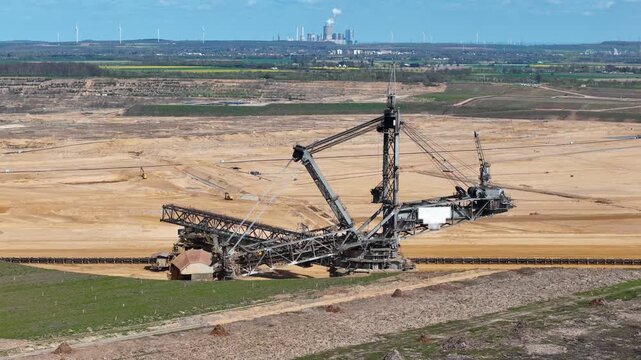 bucket wheel excavator stands before distant cooling towers wind turbines dot green farmland yellow rapeseed fields horizon lignite pit drone aerial view hambach coal mine germany infrastructure