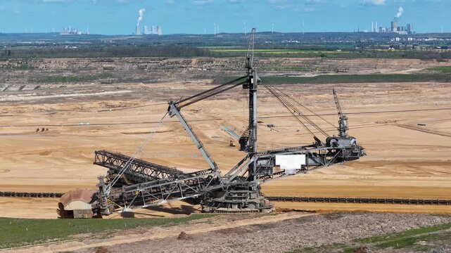 bucket wheel excavator overlooks distant cooling towers steam wind turbines line horizon farmland below lignite pit drone aerial establishing shot hambach coal mine germany energy infrastructure