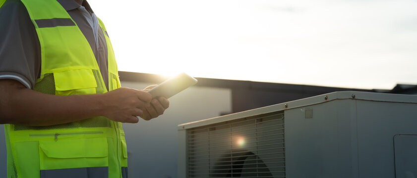 Asian maintenance engineer works on the roof of factory. contractor inspect compressor system and plans installation of air condition systems in construction. technology, online, mobile application.
