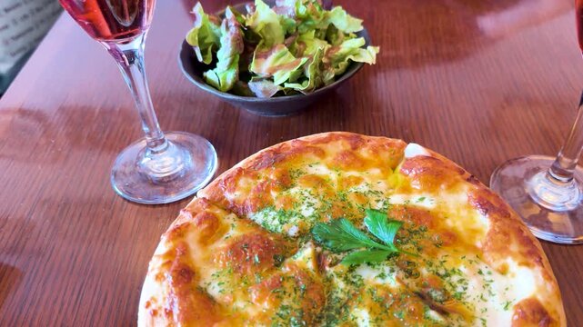 A delicious garlic cheese bread pizza served with a side salad and two glasses of rose wine on a wooden table, static high angle shot.