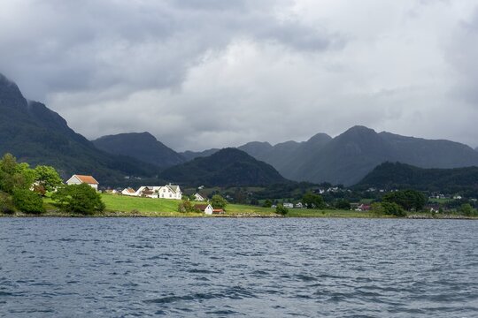 Traditional Norwegian village by Lysefjord mountains under overcast sky