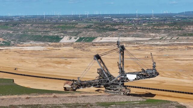 bucket wheel excavator perches above terraced lignite pit dense wind turbine array distant horizon small town edges mine boundary drone aerial view hambach coal mine germany renewable energy