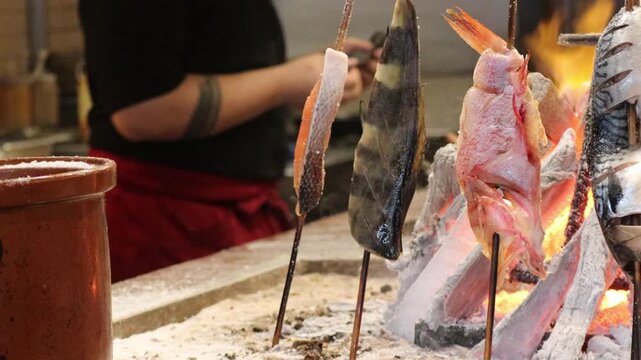 Vertical Fish and Seafood Skewers Grilling on Robatayaki Charcoal Pit in a Restaurant Setting
