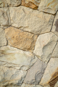 Natural stone wall surface with irregular layered rocks, visible cracks, rough textures, and subtle beige, gray, and brown tones.