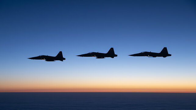 Silhouette of three military fighter jet airplanes fly in formation across a bright blue and orange sunset sky above the horizon line