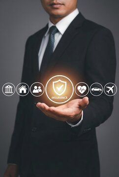 Businessman in a black suit holding glowing insurance icons in his hand with protective shield concept