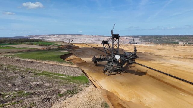 bucket wheel excavator carves hambach lignite mine terraced pit walls stretch toward green farmland wind turbines dot horizon near kerpen germany massive mining machinery surface coal extraction