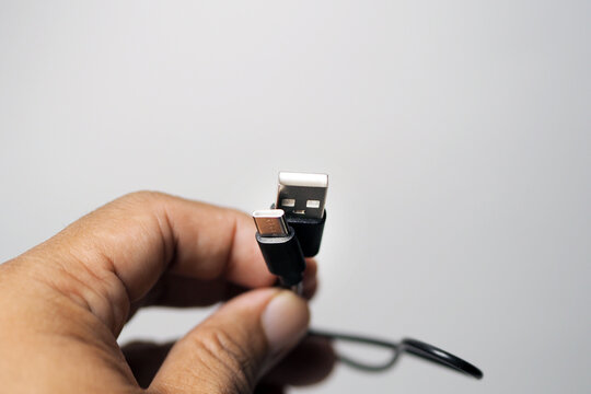 A human hand holding up two black USB cable heads against a soft neutral background.