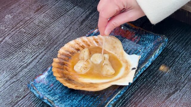 Close up footage of a scallop being picked up with a toothpick from its shell.