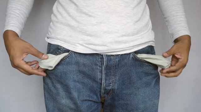 A close up shot of a man's lower torso, pulling out his empty pockets, gesturing that he does not have any money in his pockets, feeling empty and sad