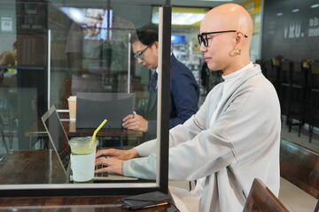 Fototapeta premium A smart-looking Korean female employee sits working with a male colleague using a smartphone and laptop in a cafe or co-working space. 