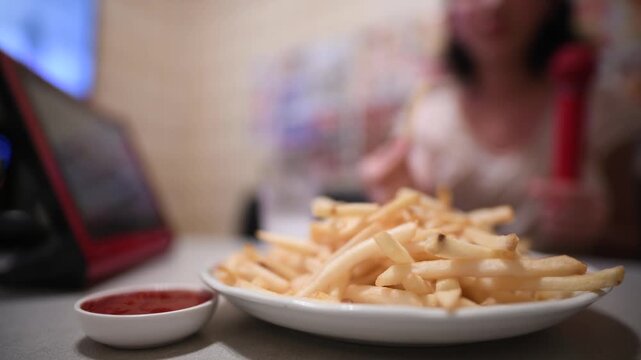 カラオケを楽しむ女性とテーブルに置かれたフライドポテト