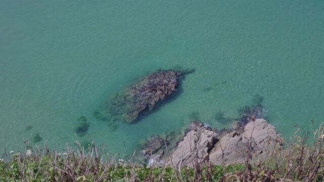 Views down from the cliffs onto the clear blue sea at Newquay, Cornwall, England on a hot sunny June day.