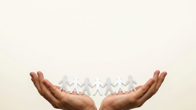 Minimalist paper people chain held in cupped hands, community support and social unity concept, white paper cutouts representing human connection