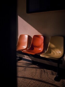 Three empty retro plastic waiting chairs in orange and yellow with dramatic sunlight and shadows