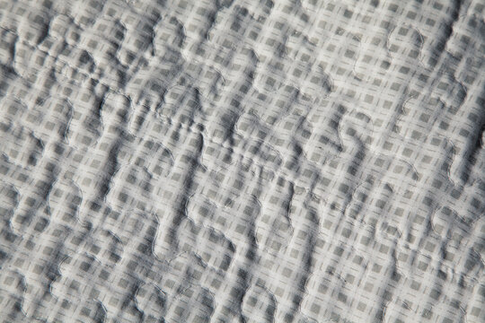 Close-up of light gray wrinkled vintage fabric with subtle checkered pattern. Soft crumpled texture of authentic cotton or linen material. Natural folds and delicate weave visible. 