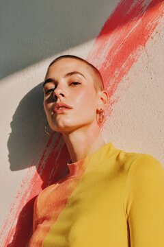 Buzz cut fashion portrait in yellow top against red brushstroke wall with hard sunlight and shadow