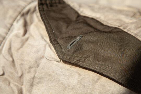 Close-up of brown vintage fabric with pocket detail and metal rivet. Authentic aged textile of jacket or coat material. Natural wrinkles, soft cotton or canvas texture and visible construction element