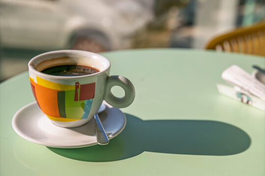 Americano coffee in a vibrant patterned cup on a mint table, with strong sunlight and a softly blurred interior.