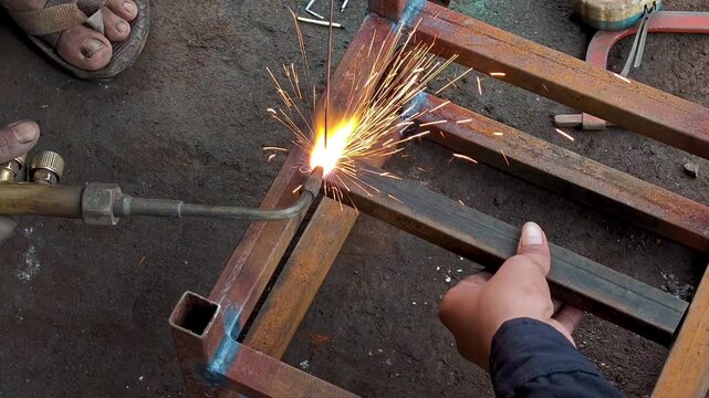 Welder gas welding metal square pipe frame with torch in workshop. Gas welding process