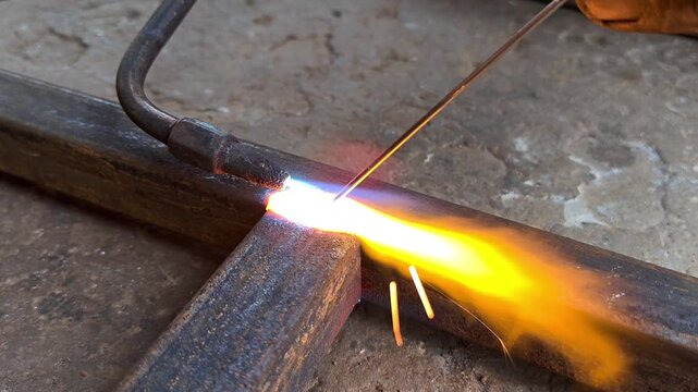 Welder gas welding metal square pipe frame with torch in workshop. Gas welding process