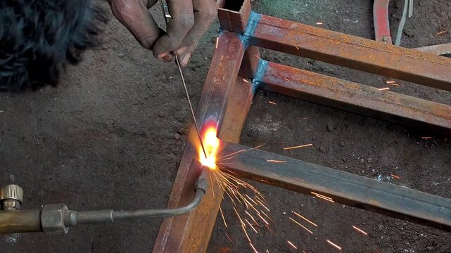 Welder gas welding metal square pipe frame with torch in workshop. Gas welding process