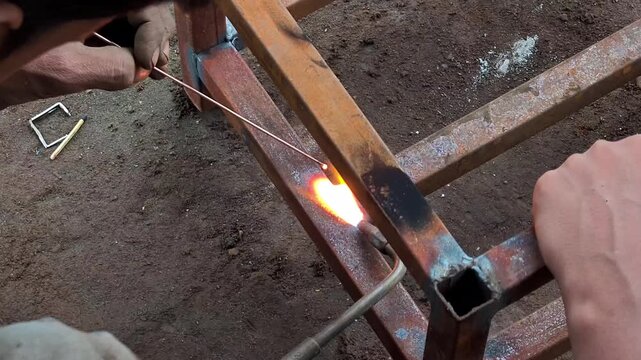 Welder gas welding metal square pipe frame with torch in workshop. Gas welding process