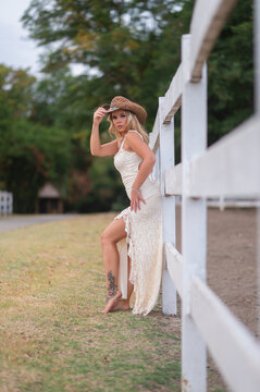 Young woman in cowgirl hat posing by white fence