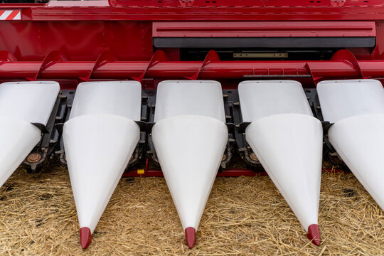 Front view of white snouts on corn header attachment of agricultural combine harvester over straw ground.