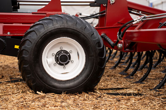 Side view of black rubber tire with white rim mounted on red agricultural implement frame over field straw.