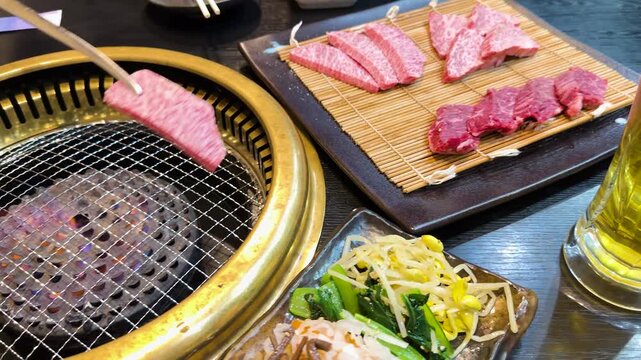 Person using metal tongs to grill premium japanese wagyu beef on charcoal barbecue in restaurant.