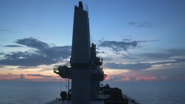 eye level view of heavy deck cargo crane silhouette against colorful after sunset sky of a bulk carrier sailing in open sea