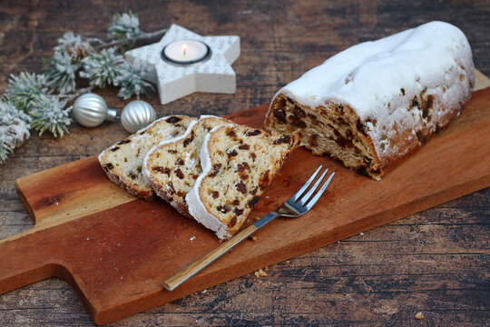 Traditioneller Weihnachtsstollen aufgeschnitten auf einem Holzbrett mit festlicher Dekoration und Kerzenschein.