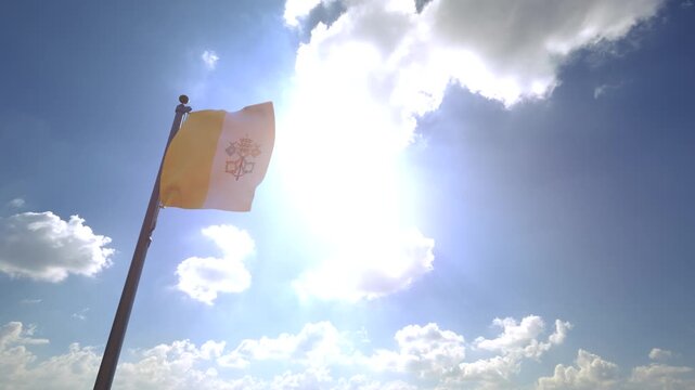 Vatican City Flag waving on a Flagpole from a Moving Angle in front of a blue sky with clouds	