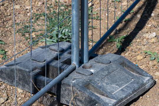 A heavy-duty black rubber base block secures portable wire mesh fencing panels upright on dry dirt ground.