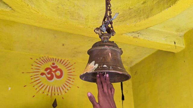 Person ringing brass bell in hindu temple with om symbol in background
