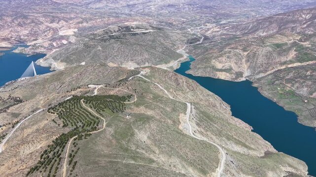 4K wide aerial drone shot flying over a mountain landscape, revealing a scenic lake, surrounding valleys, and majestic peaks. Natural lighting, color grading friendly flat profile.