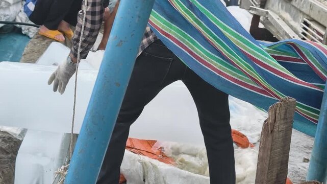 Vietnamese port worker pulling and carrying a heavy block of ice down to a fishing boat at a coastal dock in central Vietnam