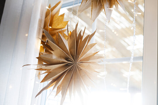 Handcrafted Paper Stars Hanging in Window with Warm Fairy Lights, Concept of Nordic Christmas Decor, Eco-Friendly Winter Interior and Cozy Lighting