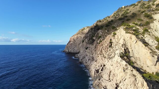 Aerial drone orbiting a coastal rock formation above the Mediterranean Sea near Benidorm, Costa Blanca, Alicante, Spain, morning.